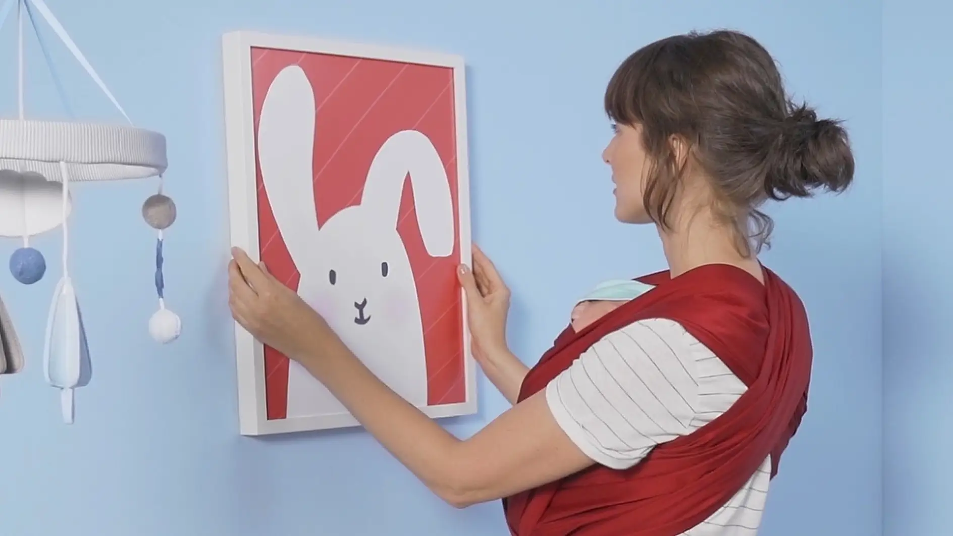 A woman is hanging up a frame with a playful children illustration.
