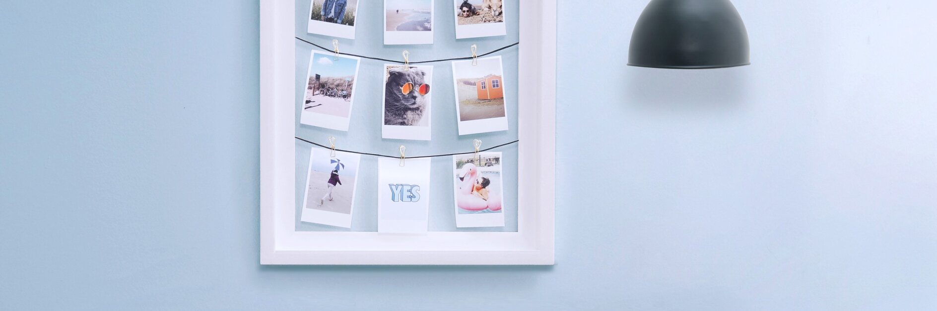 Ein Rahmen an der Wand, in dem mehrere kleine Fotos an Schnüren befestigt sind.