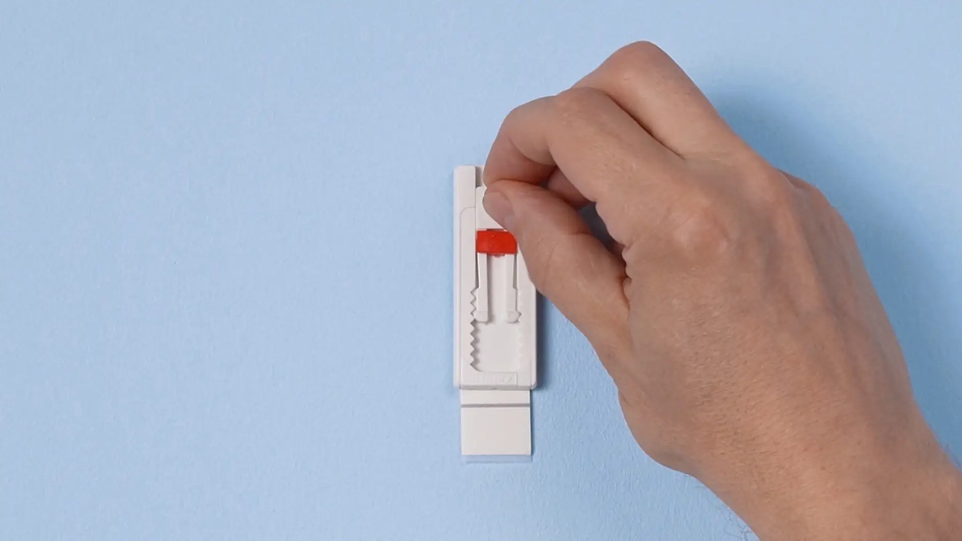 The Adjustable Adhesive Nail by tesa is mounted to the wall. A hand is adjusting the nail’s lever.
