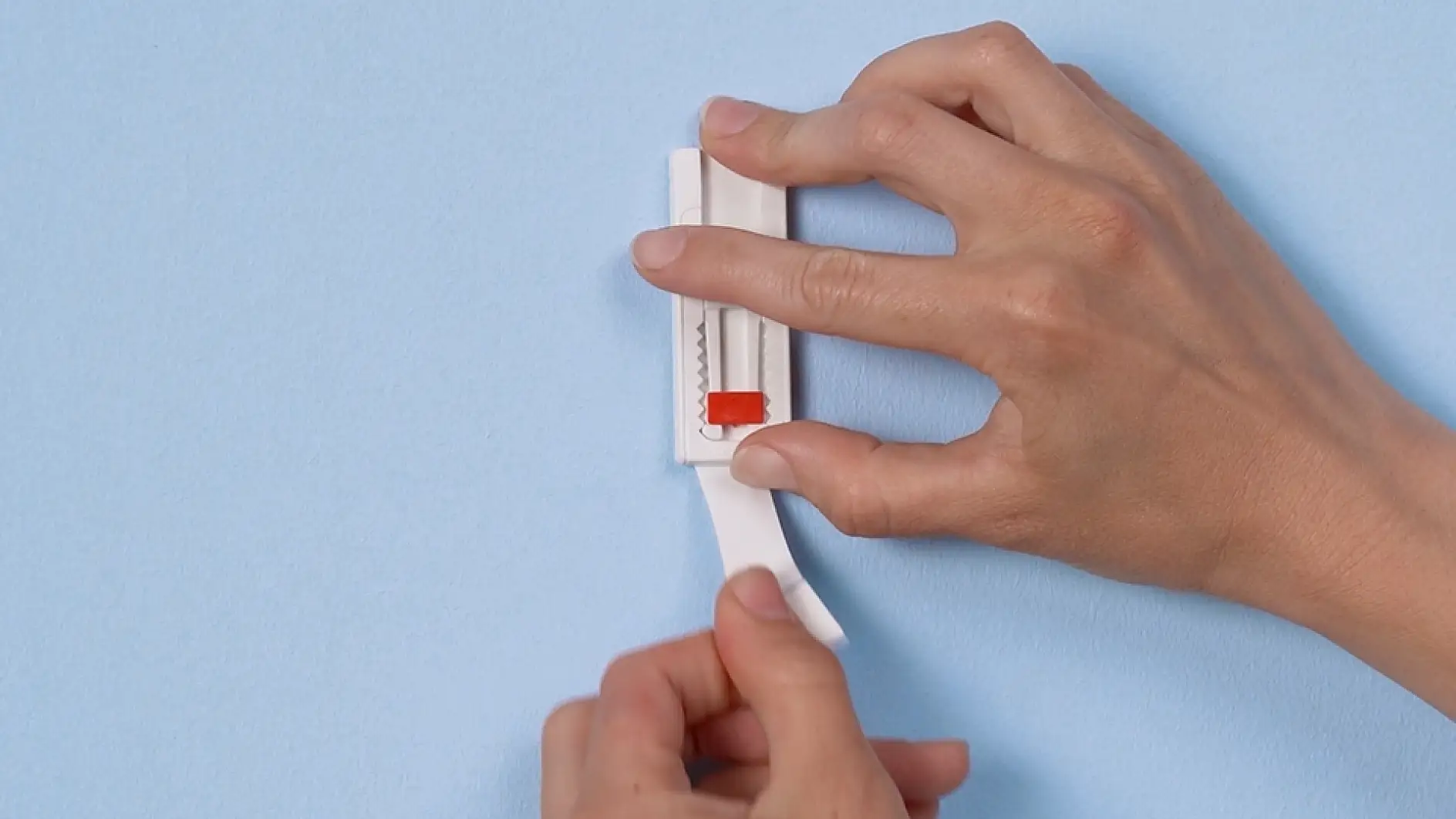 The Adjustable Adhesive Nail by tesa is mounted to the wall, a hand pulls down adhesive strip from under it
