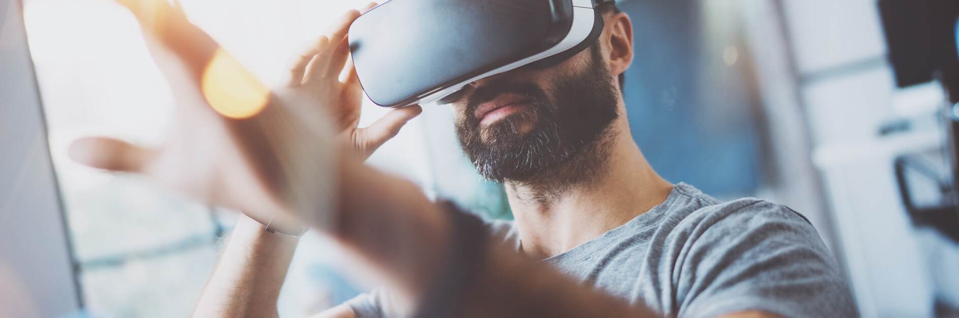 Nahaufnahme eines bärtigen jungen Mannes mit einer Virtual-Reality-Brille an einem modernen Coworking-Arbeitsplatz. Smartphone mit VR-Headset. Horizontal, verschwommen.