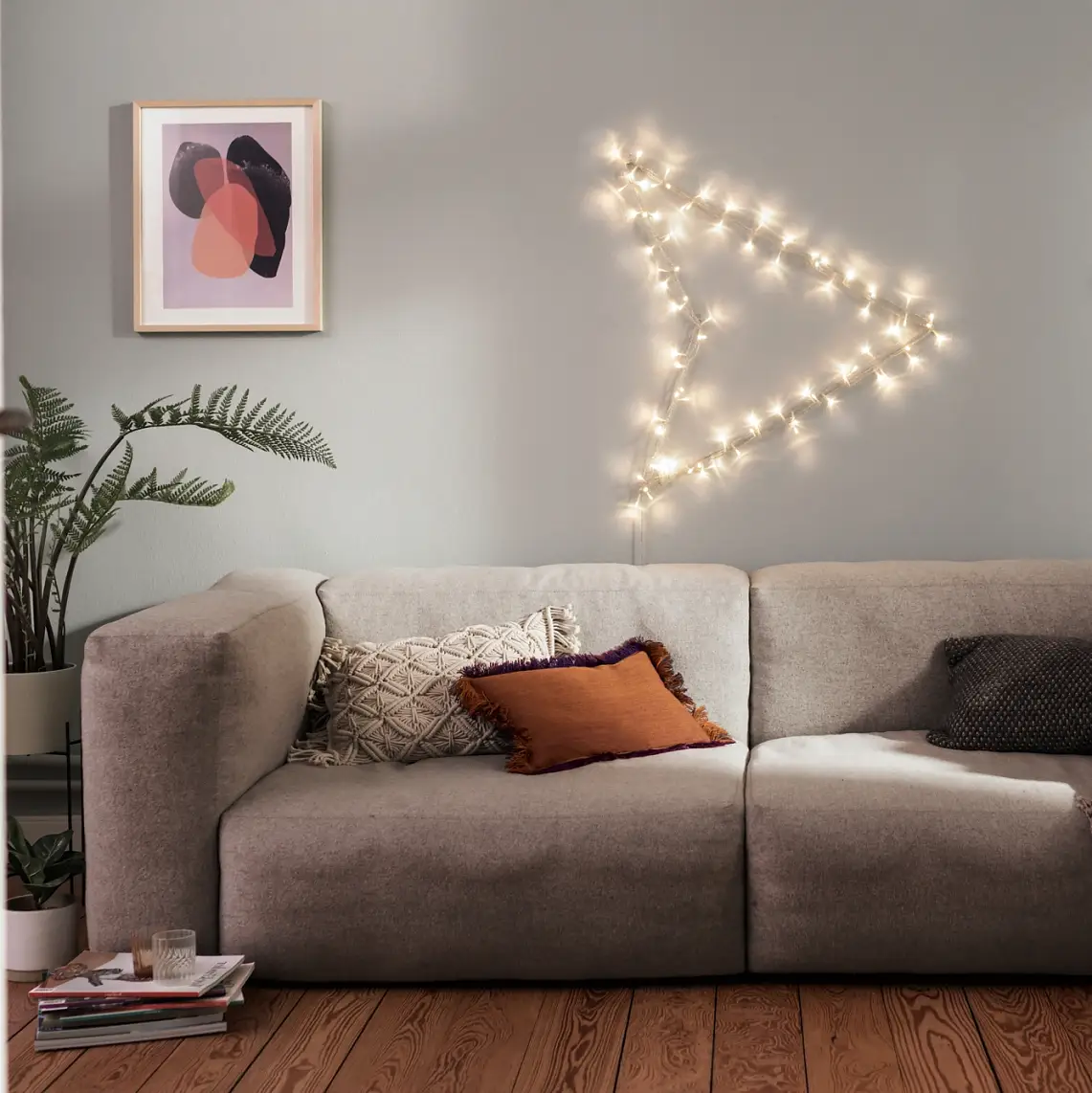 Beleuchtungsideen – Teaser: Graues Sofa in der Mitte, darüber ein beleuchteter Pfeil an der Wand.