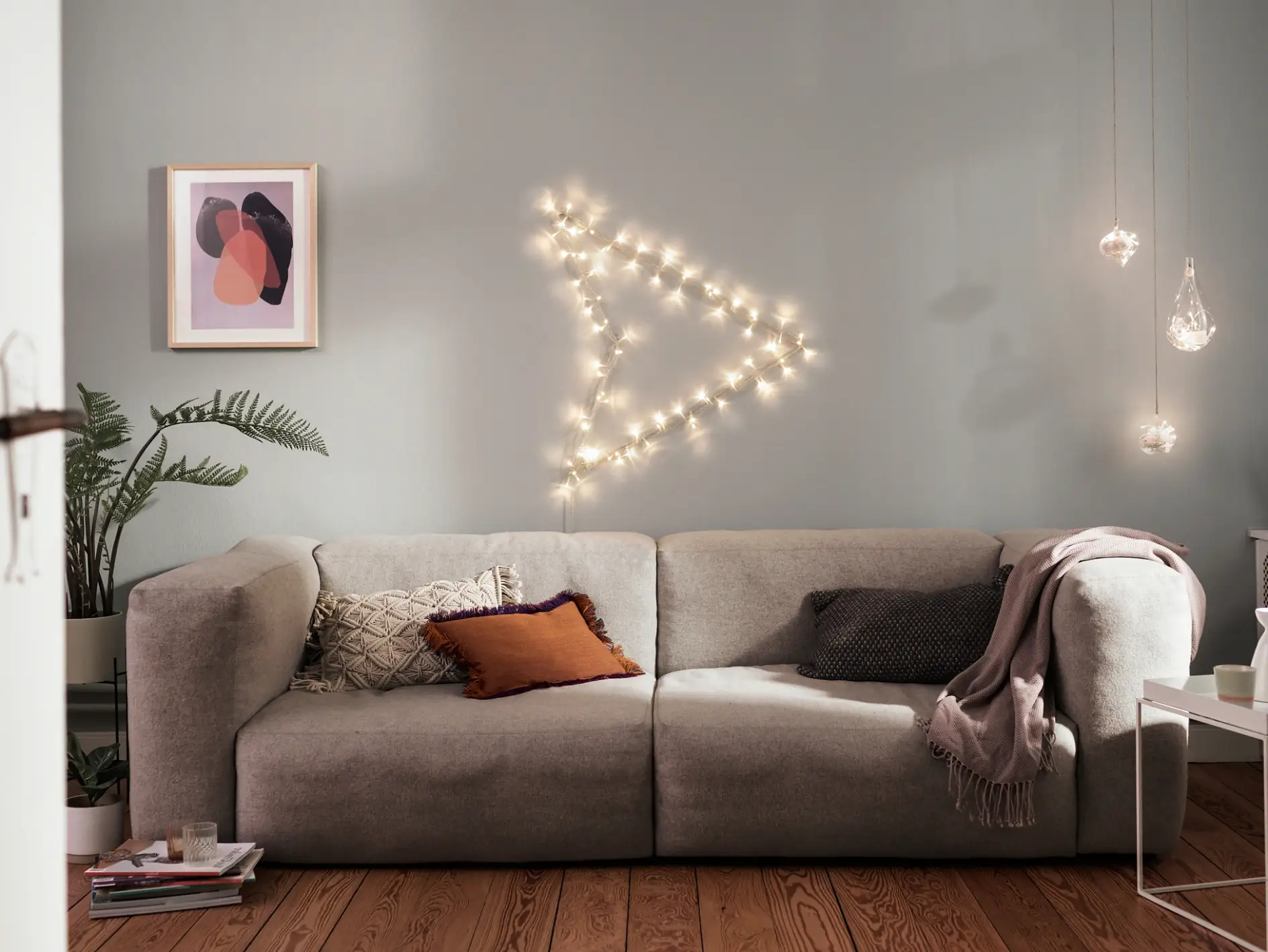 Beleuchtungsideen – Teaser: Graues Sofa in der Mitte, darüber ein beleuchteter Pfeil an der Wand.