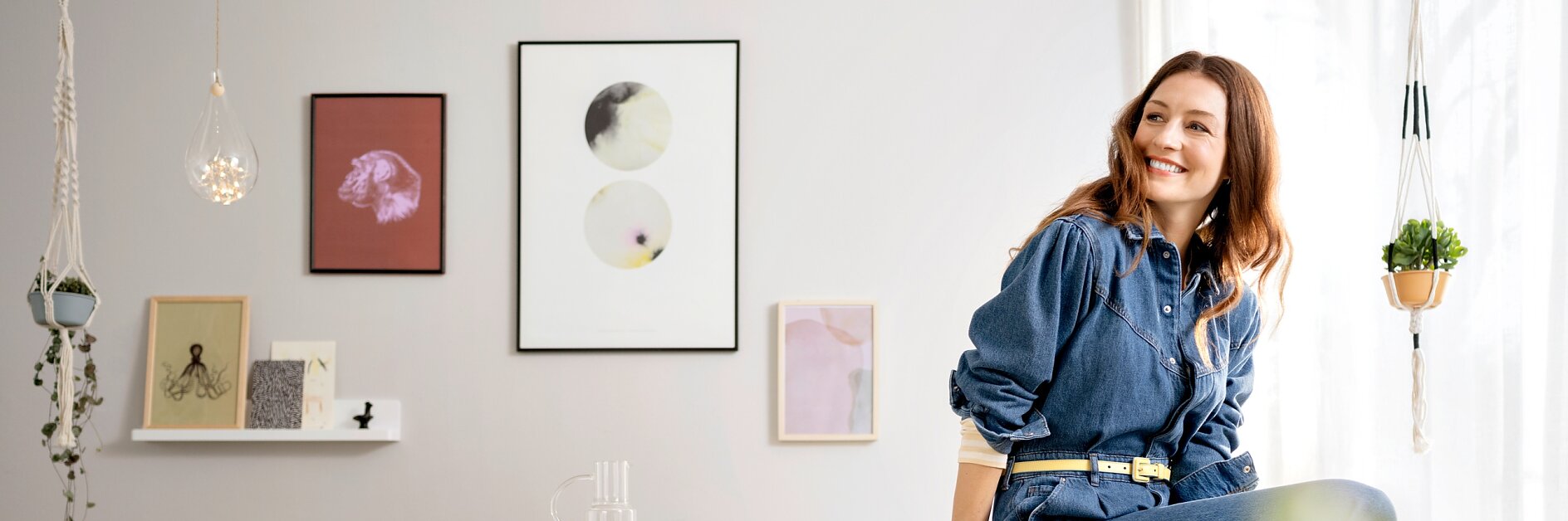 Wohnzimmer gestalten - Frau sitzt lachend auf der Kante eines Tisches, im Hintergrund Bilder