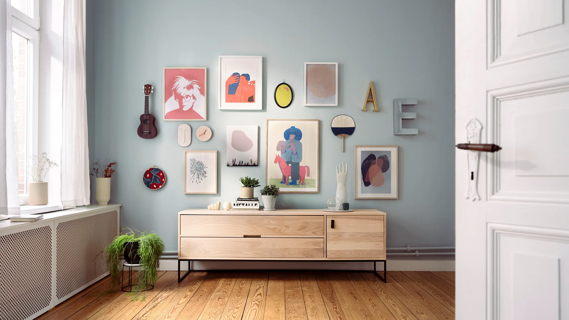 Wall Gallery – Teaser: Bilder, Buchstaben, Geige und Deko-Elemente hängen an heller Zimmerwand.