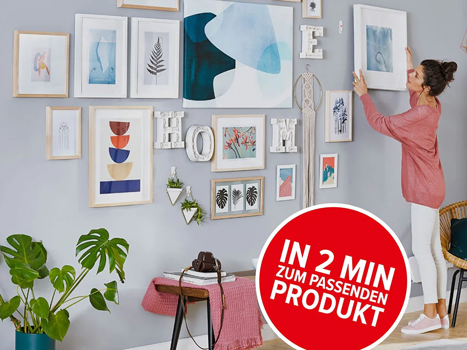Eine Frau im legeren Outfit rückt ein gerahmtes Bild an einer grauen Wand zurecht, auf der eine Collage aus abstrakter und naturbezogener Kunst zu sehen ist. Darunter steht eine rosa Bank mit einer Pflanze und einem Wählscheibentelefon. Ein roter Kreis mit deutschem Text hebt eine Werbung oder ein Produkt im Zusammenhang mit Tesa-Klebeband hervor. (This text has been generated by AI)