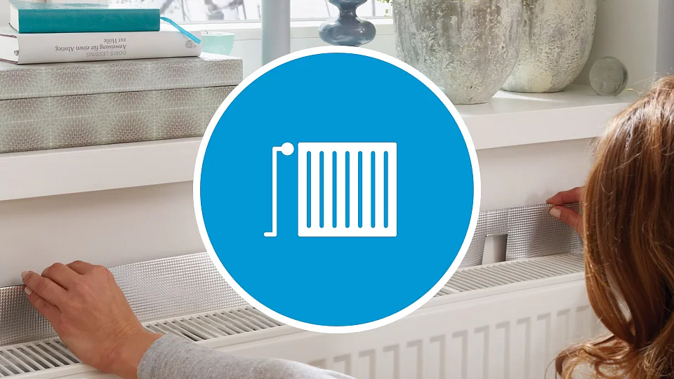 Eine Person befestigt mit Tesa-Klebeband Dämmmaterial an einem Heizkörper unter einer Fensterbank. Auf der Fensterbank stehen eine Dekopflanze und Bücher. Im Vordergrund ist ein blauer Kreis mit einem weißen Heizkörpersymbol über das Bild gelegt. (This text has been generated by AI)