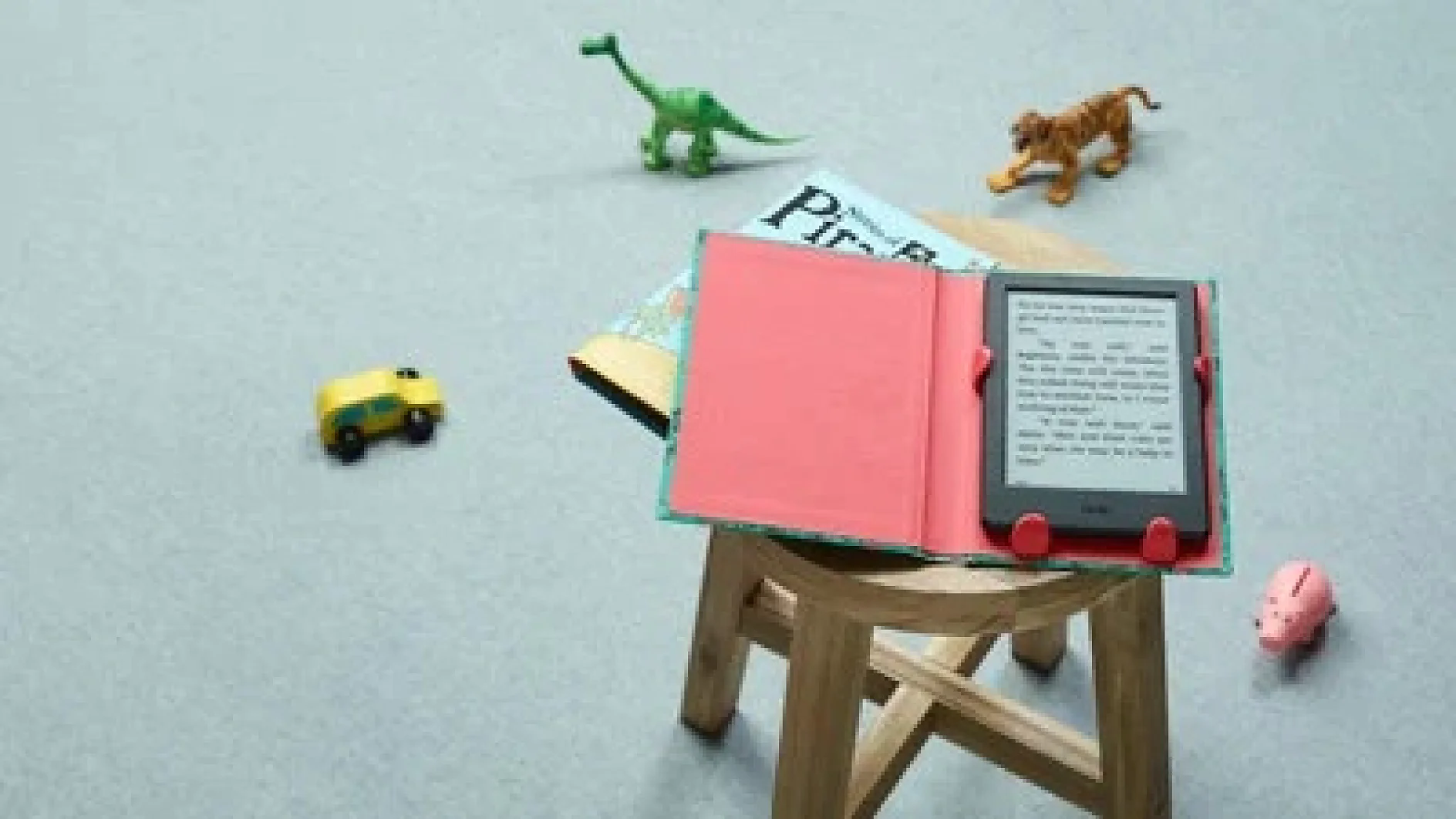 Auf einem kleinen Holzhocker stehen ein aufgeklappter E-Reader und ein Taschenbuch. Spielzeuge, darunter ein grüner Dinosaurier, ein orangefarbener Löwe, ein gelber Lastwagen und ein rosa Schwein, liegen verstreut auf dem grauen Boden. (This text has been generated by AI)