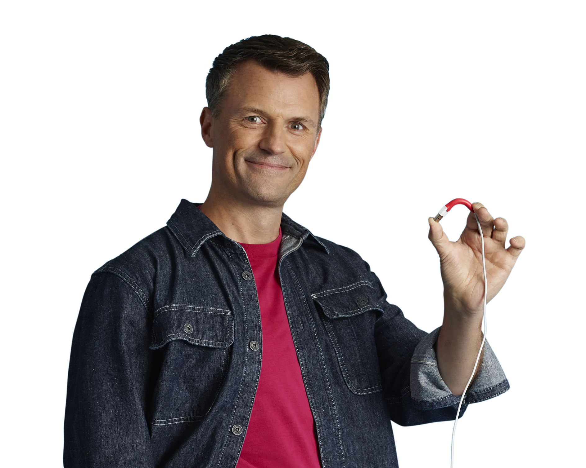 Stefan posing with cable (1) Ein Mann in einem Jeanshemd über einem roten T-Shirt lächelt in die Kamera. In seiner rechten Hand hält er ein rotes Gerät, das mit einem Tesaband verbunden ist. Der Hintergrund ist schlicht weiß. (This text has been generated by AI)