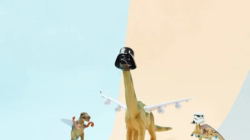 n_800_Sugru_downloadables_9-11-17_111399 Drei Dinosaurierspielzeuge sind vor einem pastellfarbenen Hintergrund angeordnet. Ein Dinosaurier mit langem Hals trägt einen schwarzen Helm, der mit Tesa-Klebeband befestigt ist, und hat Flugzeugflügel, die mit Tesa-Klebeband befestigt sind. Ein kleinerer Dinosaurier hat Boxhandschuhe, die mit Tesa-Klebeband befestigt sind, und ein anderer Dinosaurier trägt einen weißen Helm, der mit Tesa-Klebeband befestigt ist, und steht auf einem Skateboard, das mit Tesa-Klebeband an der Oberfläche befestigt ist. (This text has been generated by AI)