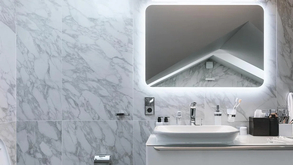 badezimmer-dekorieren_1280x1280 Ein modernes Badezimmer mit Marmorwand und einem großen, beleuchteten rechteckigen Spiegel über einer weißen Waschtischplatte. Auf der Waschtischplatte befinden sich ein rechteckiges Waschbecken, ein Seifenspender und verschiedene Toilettenartikel. Eine mit Tesa-Klebeband befestigte Toilettenecke ist sichtbar. (This text has been generated by AI)