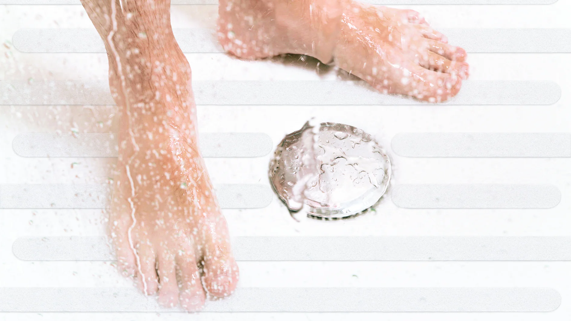 A pair of feet stands under running water in a shower. Water splashes around, and a silver drain is visible on the shower floor. The surface is lightly textured with parallel lines for grip, thanks to the innovative use of tesa tape for added traction. (This text has been generated by AI)