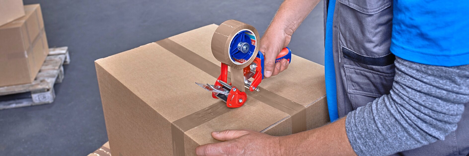 Ein Lagerarbeiter verschließt einen Karton mit braunem Tesa-Verpackungsband. Der Arbeiter verwendet einen Tesa-Klebebandabroller und trägt ein blaues Hemd mit einer grauen Weste. Im Hintergrund sind Regale mit verschiedenen Kartons und Gegenständen zu sehen. (This text has been generated by AI)
