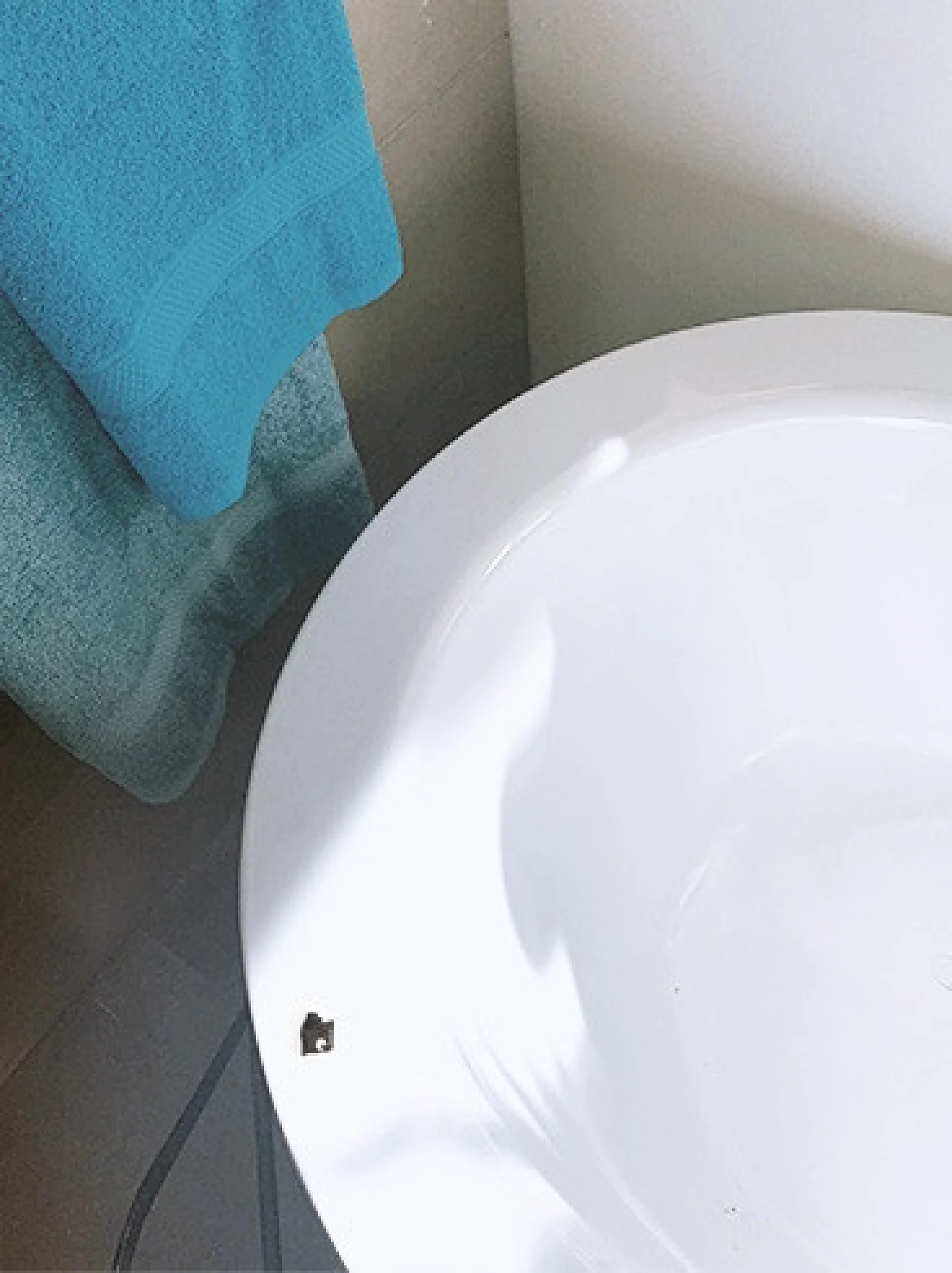 abgeplatzte-keramikJ5V8Cmt3Vkzqv_800x800 Unten rechts ist ein Teil einer weißen Badewanne mit einem kleinen Sprung zu sehen. Ein türkisfarbenes Handtuch hängt an einer Stange in der Nähe vor einer hellen Wand. Schatten auf der Oberfläche der Wanne deuten auf natürliches Licht hin, das von links kommt. (This text has been generated by AI)