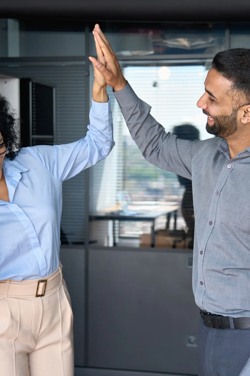 Multiracial colleagues giving high five celebrating project achievements. Cheerful successful coworkers colleagues indian businessman and African American businesswoman giving high five celebrating project victory in modern office. Business corporate culture concept.