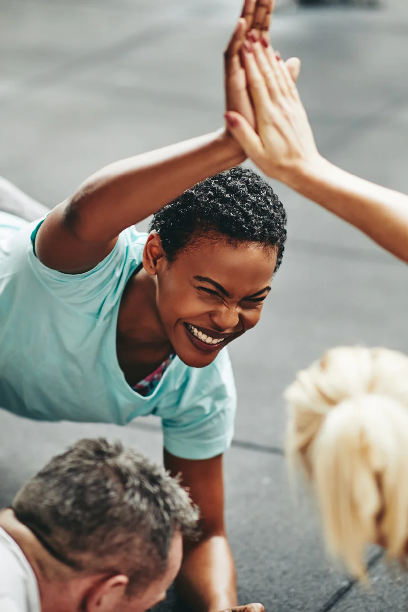 Two fit young women in sportswear laughing and high fiving while planking with a couple of male friends on the floor of a gym