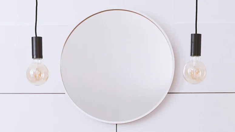 fliesenfugen-ausbessernPVS9WYdemIOvK_800x800 An einer weiß gefliesten Wand hängt ein runder, rahmenloser Spiegel, befestigt mit Tesa-Klebeband. Zwei Pendelleuchten mit schwarzen Fassungen sind symmetrisch auf beiden Seiten des Spiegels aufgehängt. Das Gesamtdesign ist minimalistisch und modern. (This text has been generated by AI)
