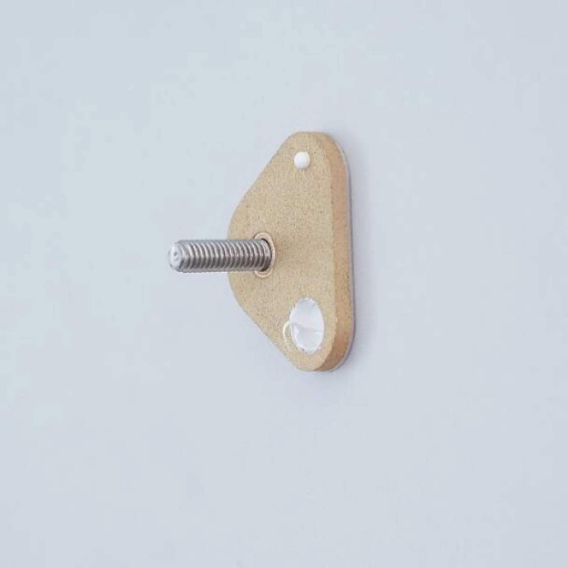 Eine dreieckige beige Wandhalterung, die an einer grauen Wand befestigt ist und in der Mitte eine hervorstehende silberne Schraube aufweist, die sicher mit Tesaband gehalten wird. (This text has been generated by AI)