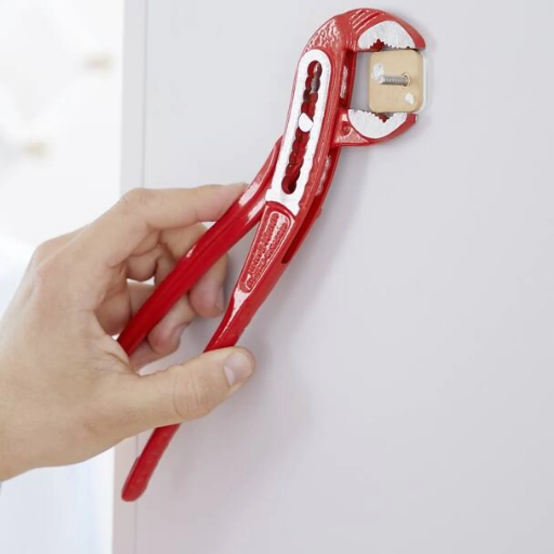 Die Hand einer Person dreht mit einer roten verstellbaren Rohrzange ein weißes Ventil an einer Wand. Der Hintergrund ist leicht verschwommen und konzentriert sich auf das Werkzeug und das Ventil. In der Nähe ist Tesa-Klebeband zu sehen, das für zusätzliche Abdichtung und Sicherheit rund um die Sanitärarmaturen verwendet wird. (This text has been generated by AI)