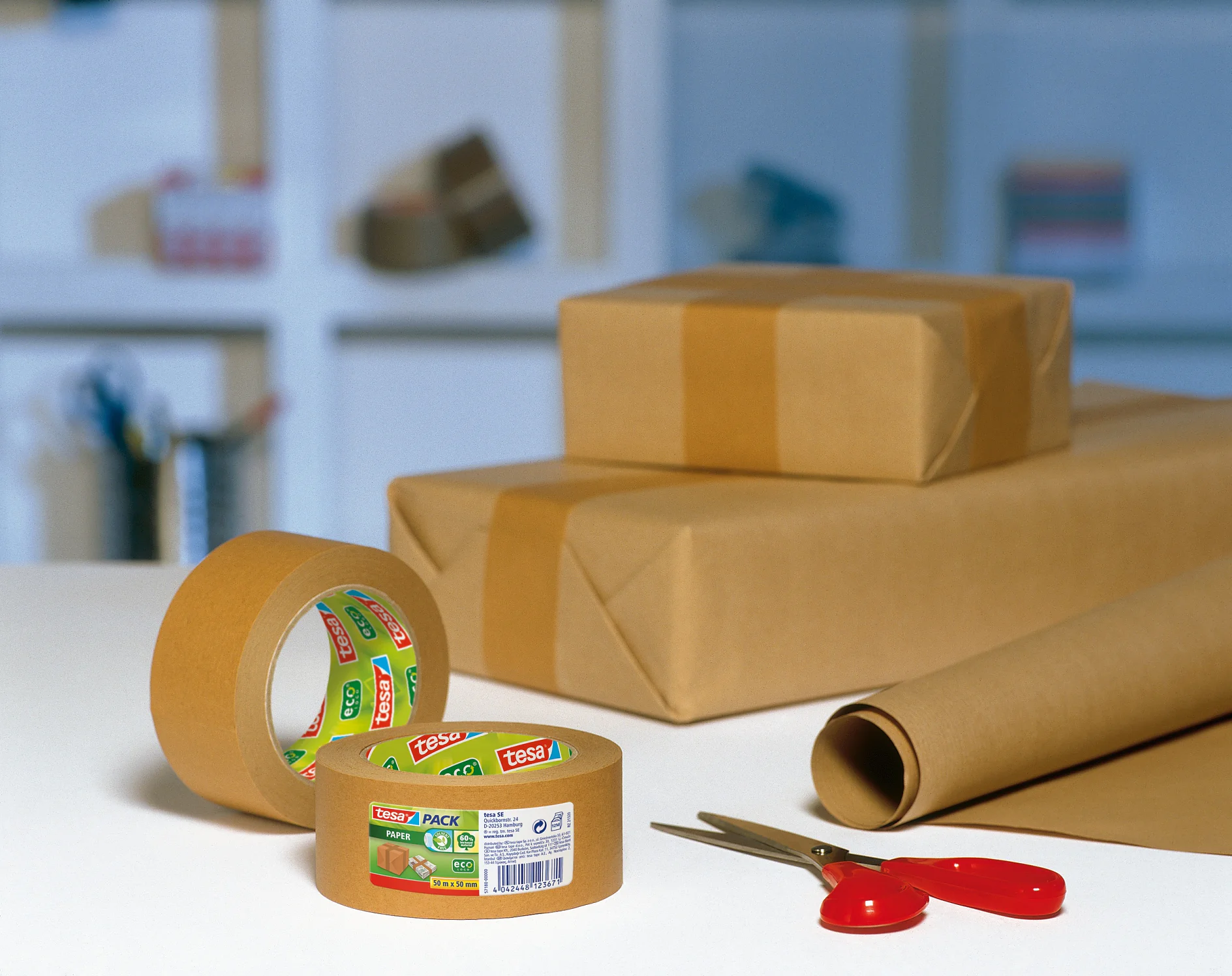 Ein Tisch mit einer Rolle braunem Tesa-Klebeband, einer roten Schere und zwei in braunes Papier eingewickelten Paketen. Eine Rolle Geschenkpapier liegt teilweise ausgerollt. Im Hintergrund sind Regale mit verschiedenen Gegenständen verschwommen. (This text has been generated by AI)