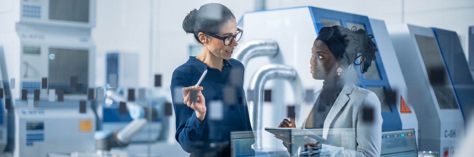 Wirtschaftsingenieur im Gespräch mit Projektleitern, sie verwenden digitale Tablet-Computer und diskutieren über moderne Fabrikplanung. Fertigungsanlage mit CNC-Maschinen und Roboterarm-Montagelinie