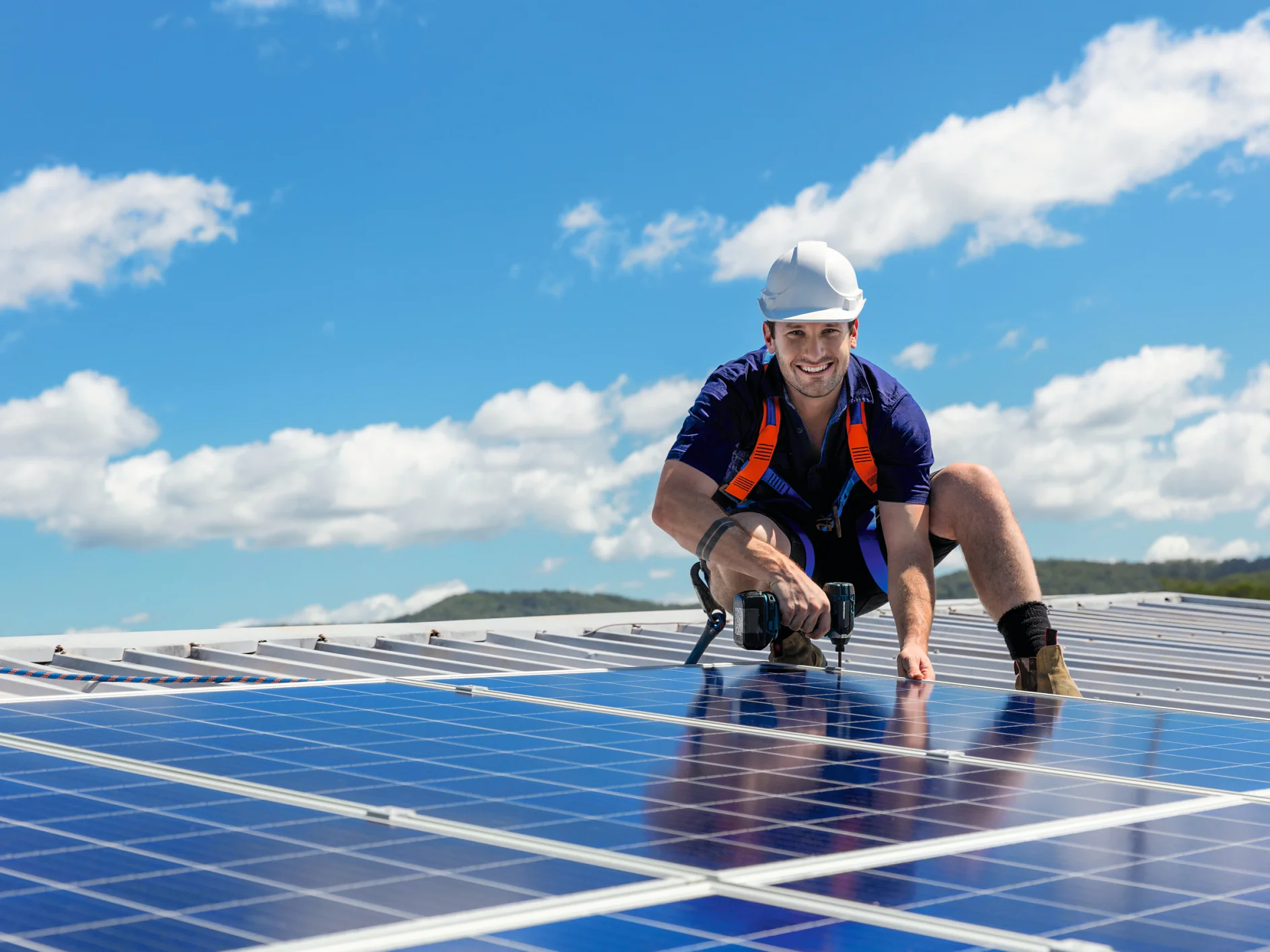 Solar panel technician with drill installing solar panels on roof on a sunny day