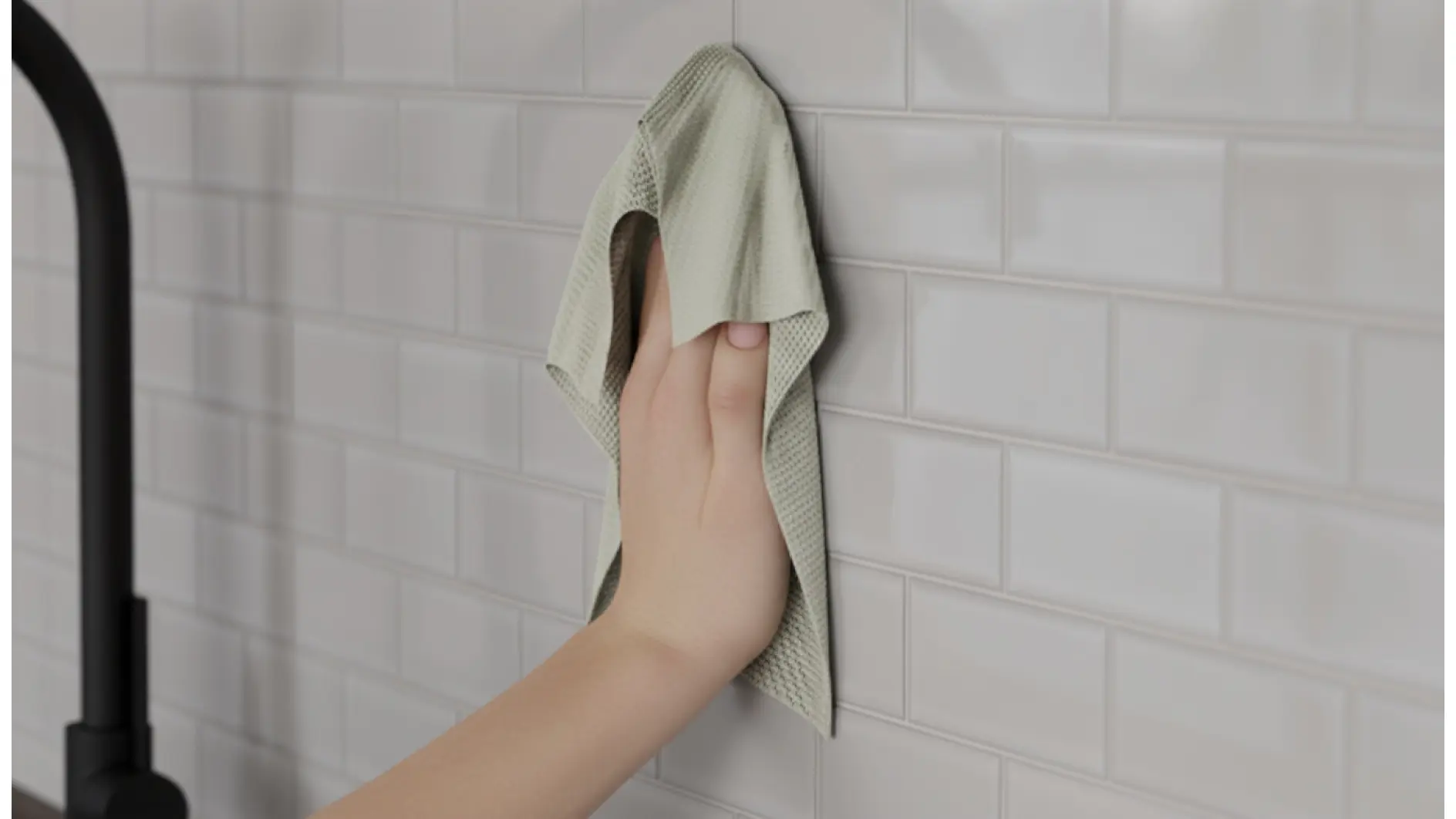 Eine Hand wischt mit einem hellen Tuch weiße U-Bahn-Fliesen an einer Wand ab, wahrscheinlich um die Oberfläche für Tesaband vorzubereiten; links ein dunkler Wasserhahn. (This text has been generated by AI)