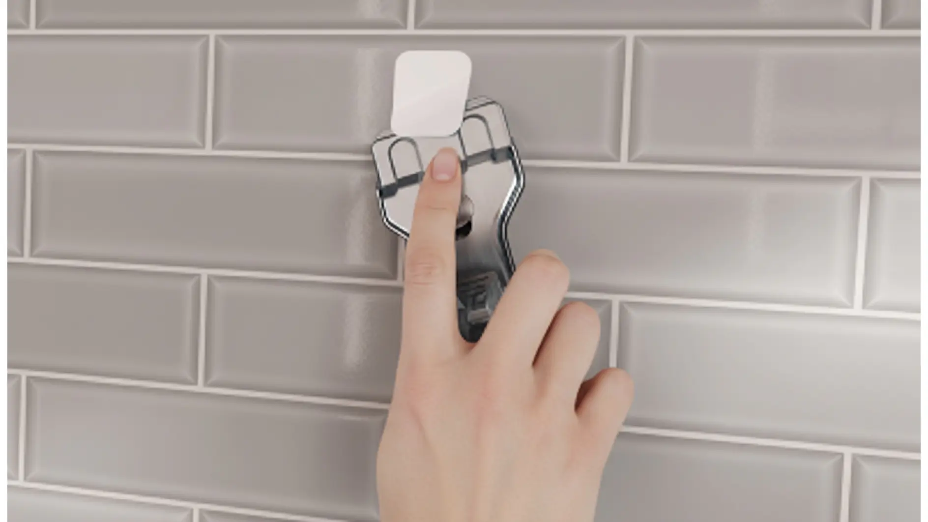 Eine Hand drückt einen durchsichtigen Wandhaken mit Tesafilm auf eine graue Kachelwand und fixiert ihn mit dem Zeigefinger. (This text has been generated by AI)