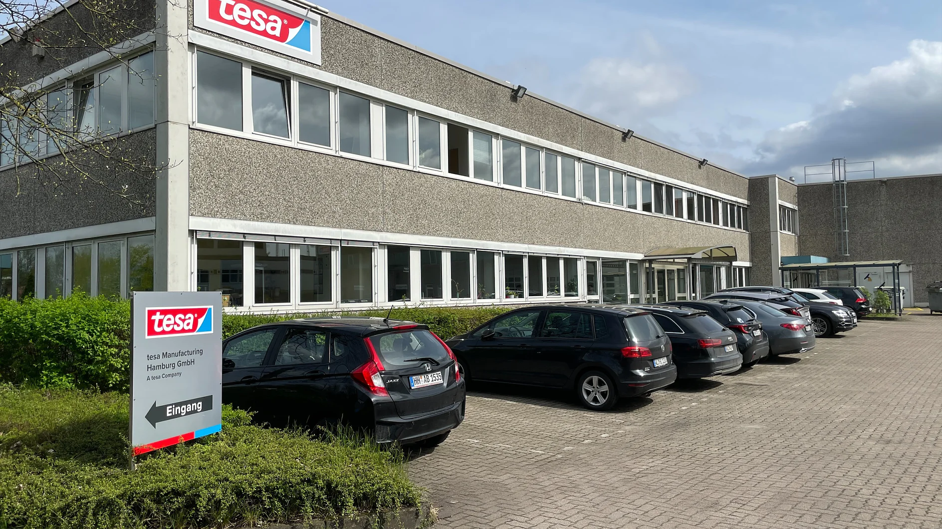 tesa Produktionsgebäude Hamburg mit geparkten Autos davor und Wegweiser am Eingang