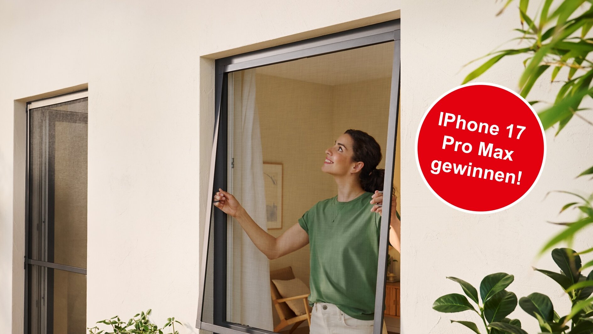 Eine Frau in einem grünen Hemd öffnet eine Fensterscheibe in einem modernen Haus. Draußen stehen Grünpflanzen, und auf einem runden Schild steht: "iPhone 17 Pro Max gewinnen!" (This text has been generated by AI)
