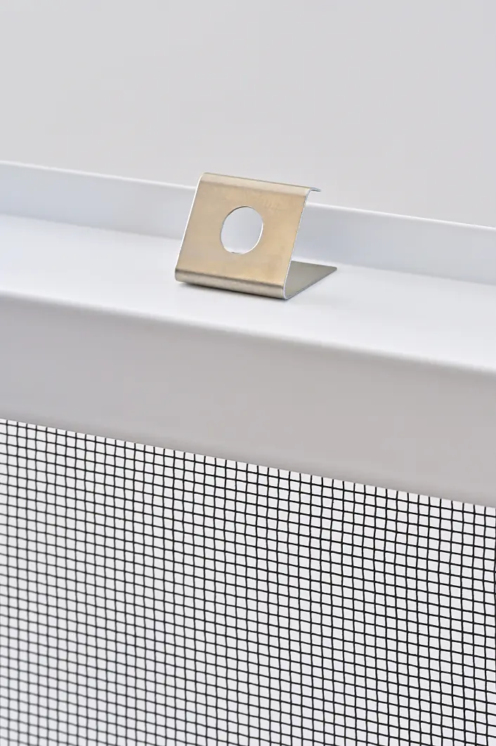 Nahaufnahme einer Metallklammer, die an der Oberkante eines weißen Fenster- oder Fliegengitterrahmens mit schwarzem Drahtgeflecht befestigt ist und mit tesa-Klebeband fixiert wird. Der Hintergrund ist einfarbig und unscharf. (This text has been generated by AI)