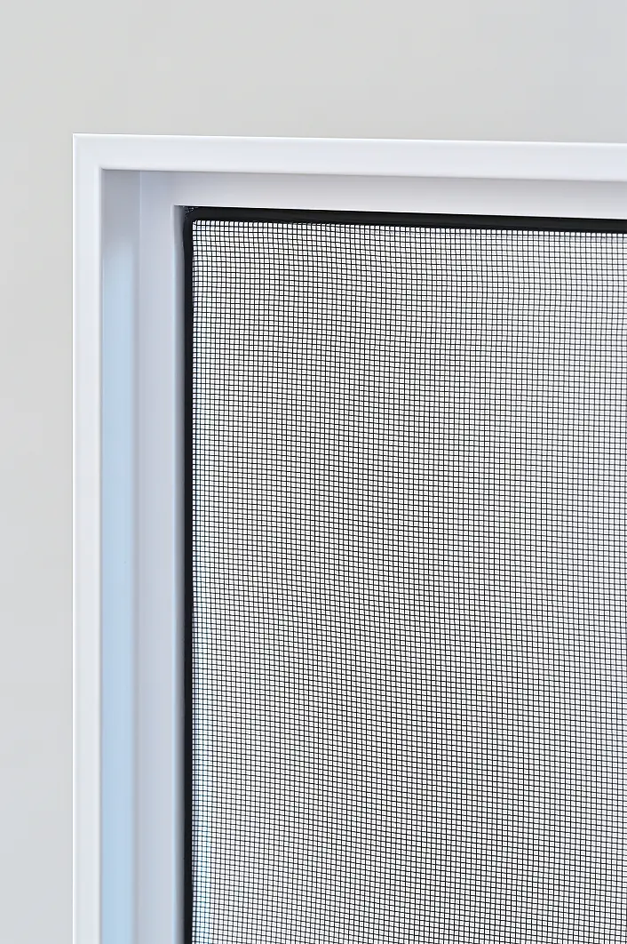 Eine Nahaufnahme eines Fenstergitters in einem weißen Rahmen, dessen dicht gewebtes Netz ein Gittermuster bildet. Das Gitter scheint in der rechten oberen Ecke leicht gewölbt oder verbogen zu sein, und im Hintergrund ist eine schlichte, helle Wand zu sehen. Auf dem Bild ist kein tesa-Klebeband zu erkennen. (This text has been generated by AI)