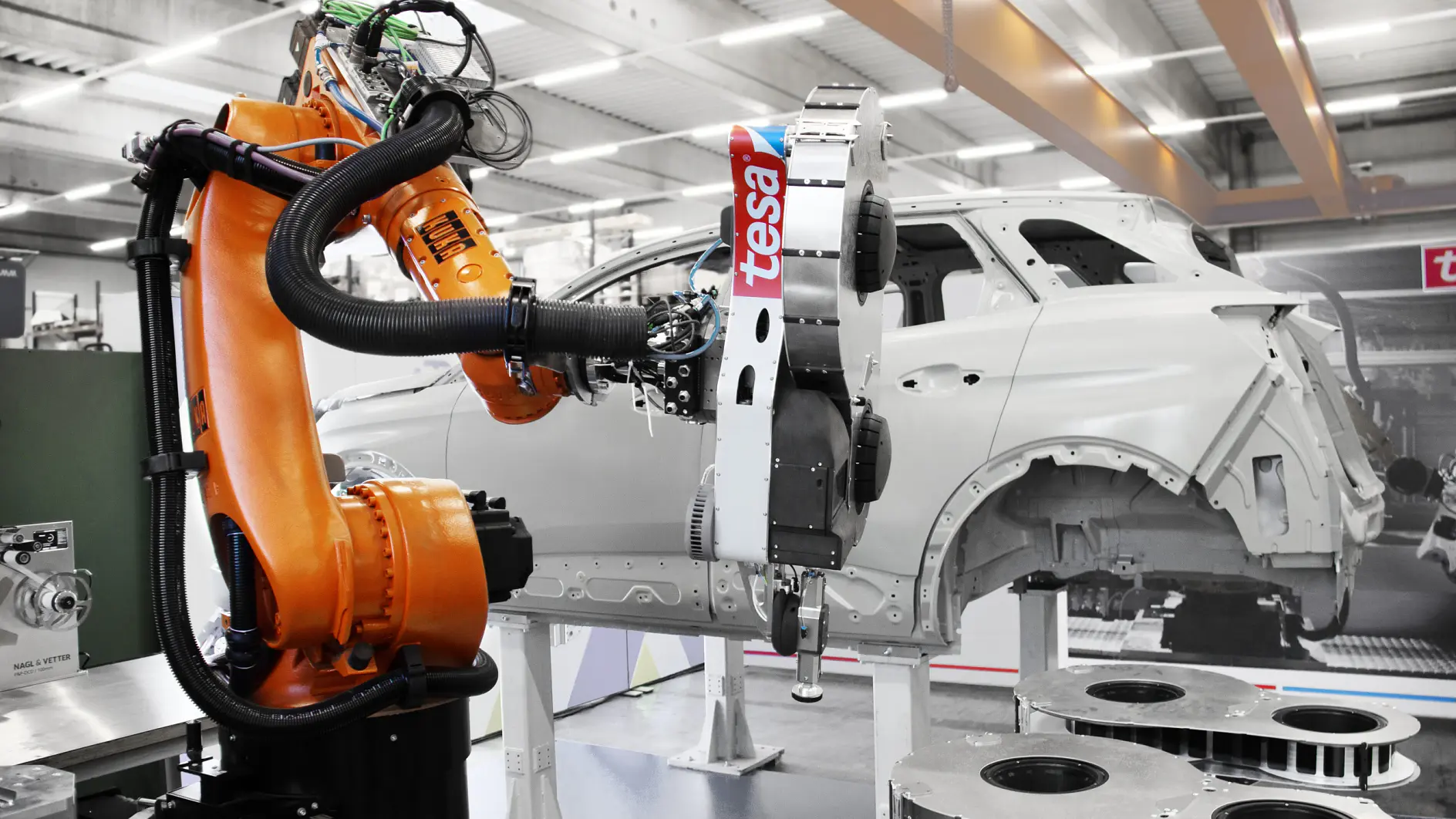 Ein Roboterarm arbeitet in einer Automobilfabrik und montiert ein teilweise gebautes Fahrzeug. Die Szene zeigt verschiedene mechanische Komponenten und Industrieanlagen unter hellen Deckenleuchten.