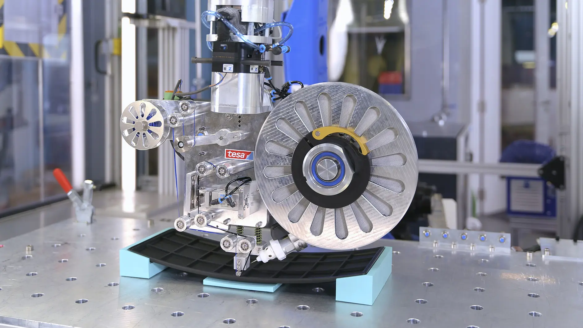 tesa-markierte industrielle Maschinenkomponente, montiert auf einer Metallplattform in einer Fabrikumgebung