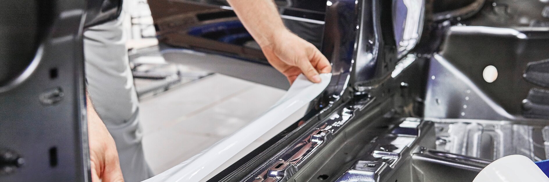 hands applying tesa adhesive tape to the interior frame of a car door in an indoor workshop setting