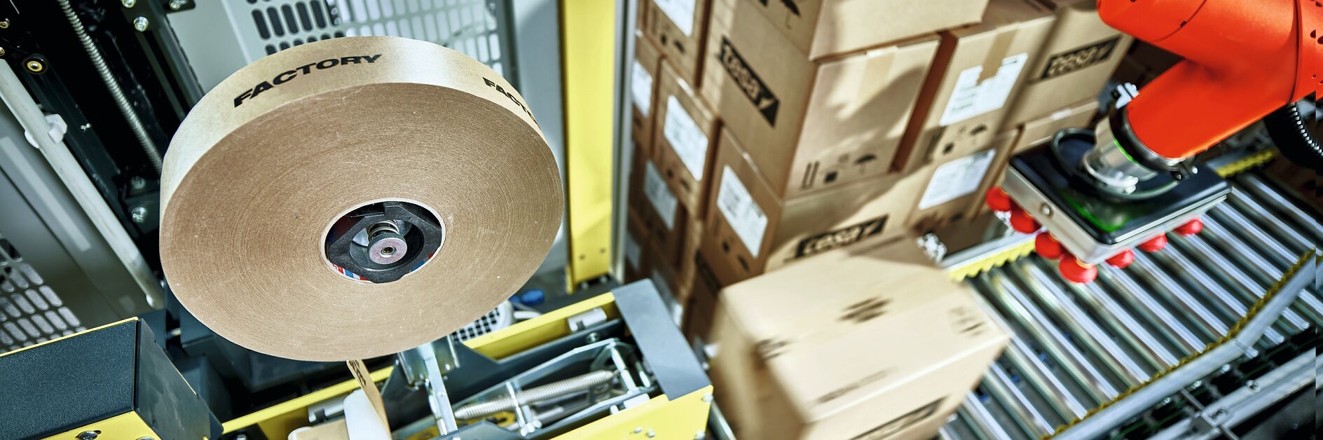 tesa tape roll near robotic arm placing cardboard boxes on conveyor belt in an industrial warehouse setting