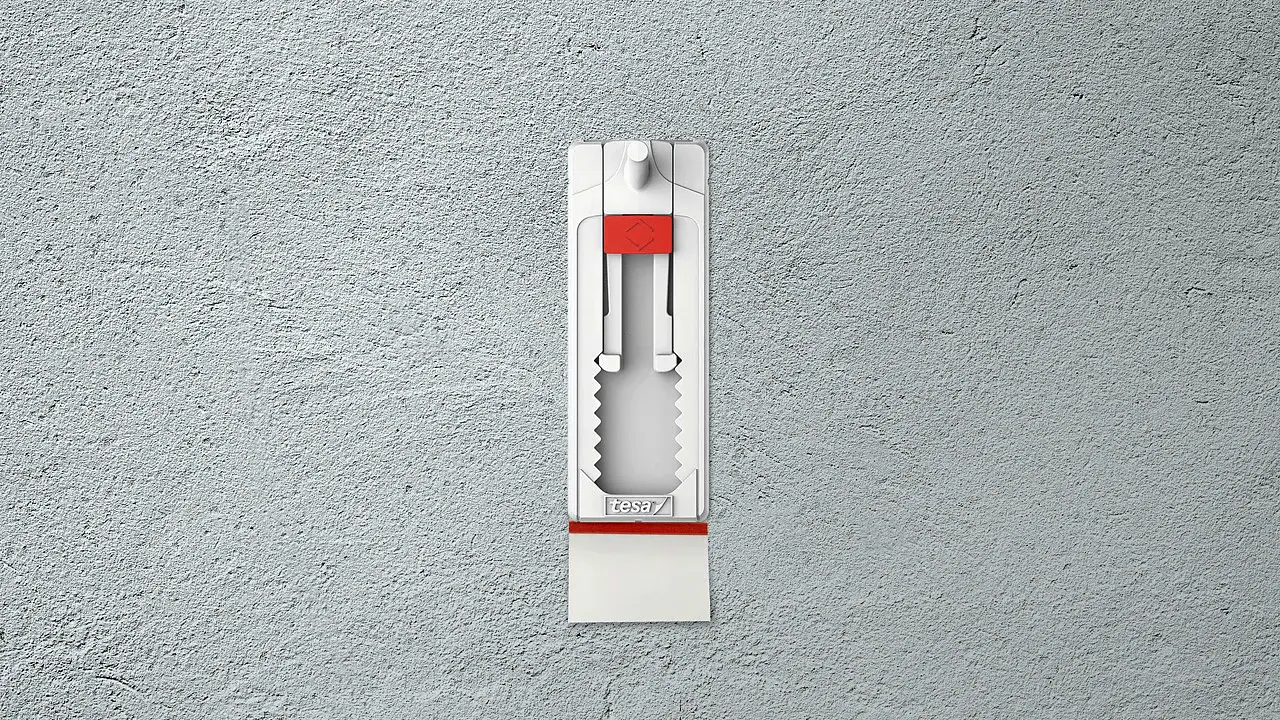Αυτοκόλλητο γαντζάκι τοίχου τοποθετημένο σε επιφάνεια με υφή, με την ταινία αφαίρεσης τραβηγμένη για εύκολη αποκόλληση χωρίς ζημιές. (This text has been generated by AI)