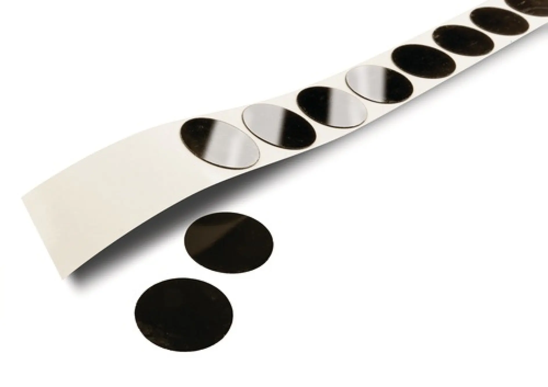 A strip of circular black tesa tape dots partially unrolled on a white surface, with two separate tesa tape dots placed next to it.