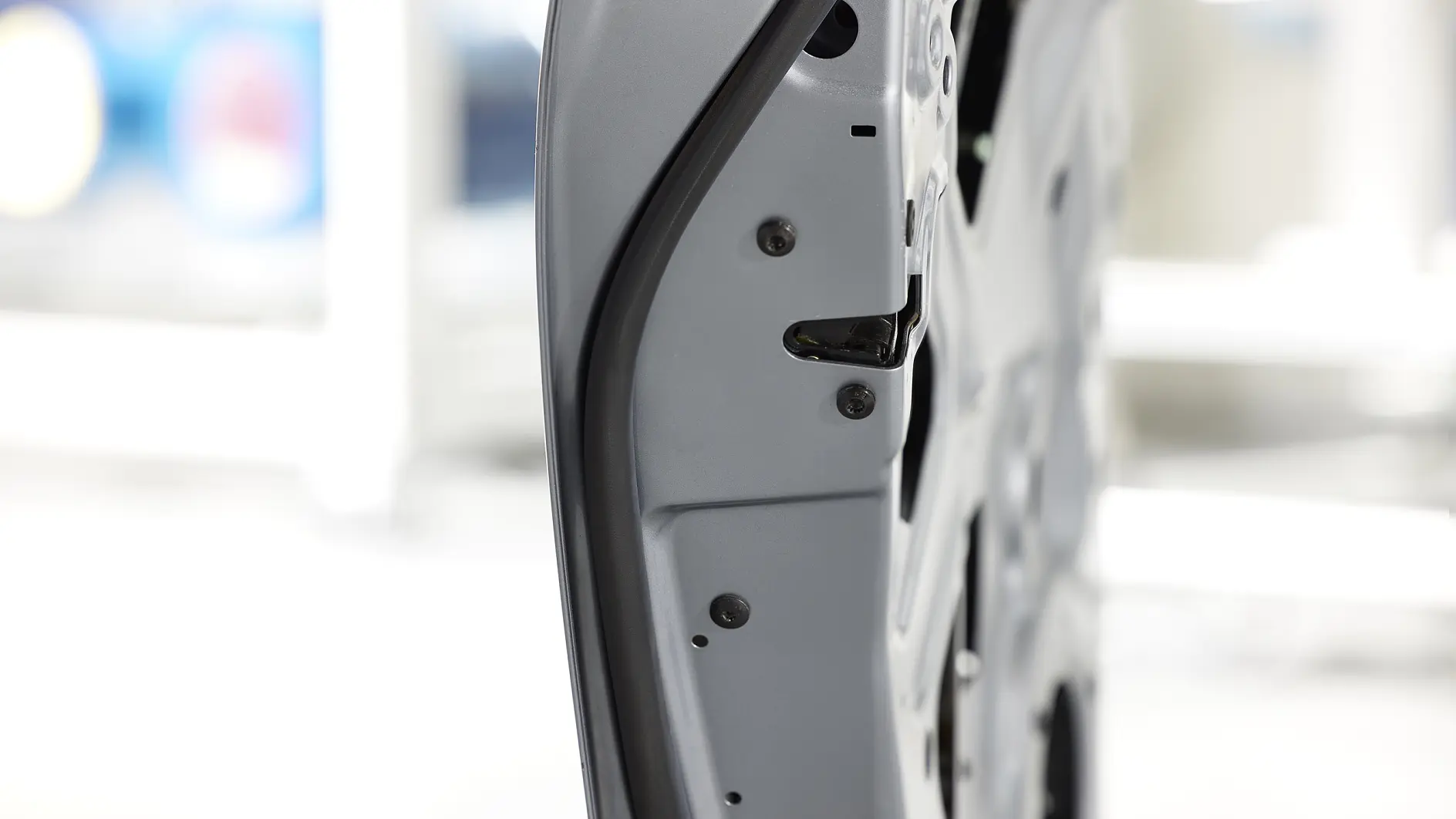 Close-up of a car door edge, showing the latch mechanism and weather stripping. The interior panel is visible, with a white background providing a clear view of the doors structure. The tesa tape used in the assembly ensures that the components are securely fastened and well-protected.