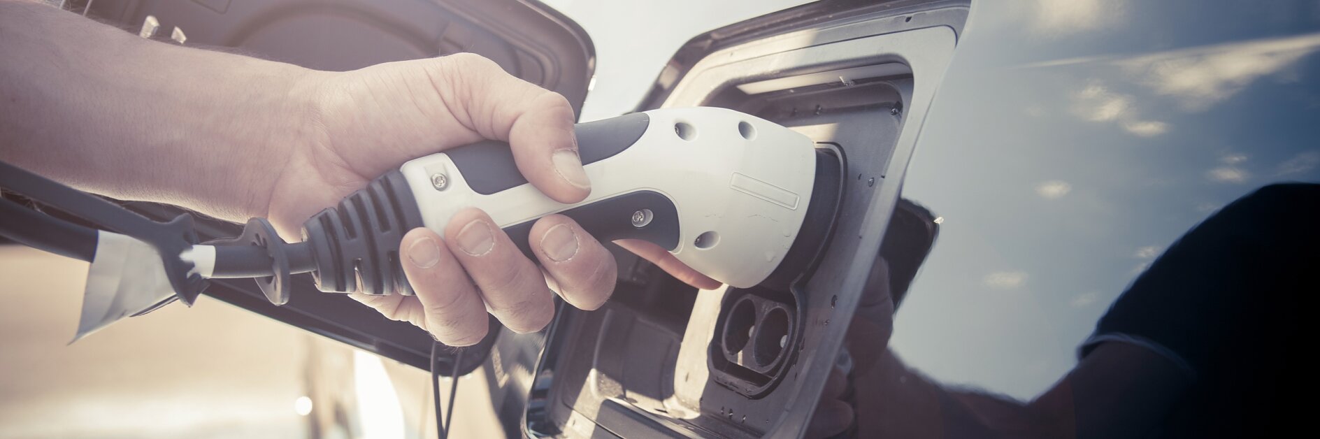 Color image of a man's hand preparing to charge an electric car.