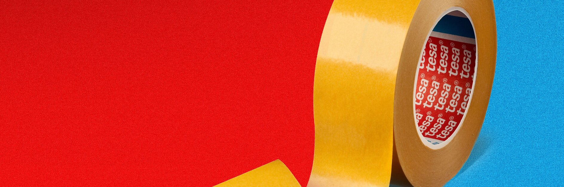 A roll of yellow tesa tape stands upright against a red and blue split background. The loose end of the tesa tape curls outward. The inside of the roll has a red label with white text.