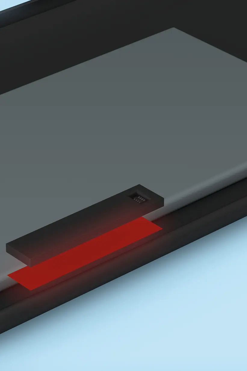 Close-up of a smartphone charger with a rectangular charging pad and a small LED indicator glowing red. The pad is placed on a black surface, likely the back of a phone, against a light blue background. (This text has been generated by AI)