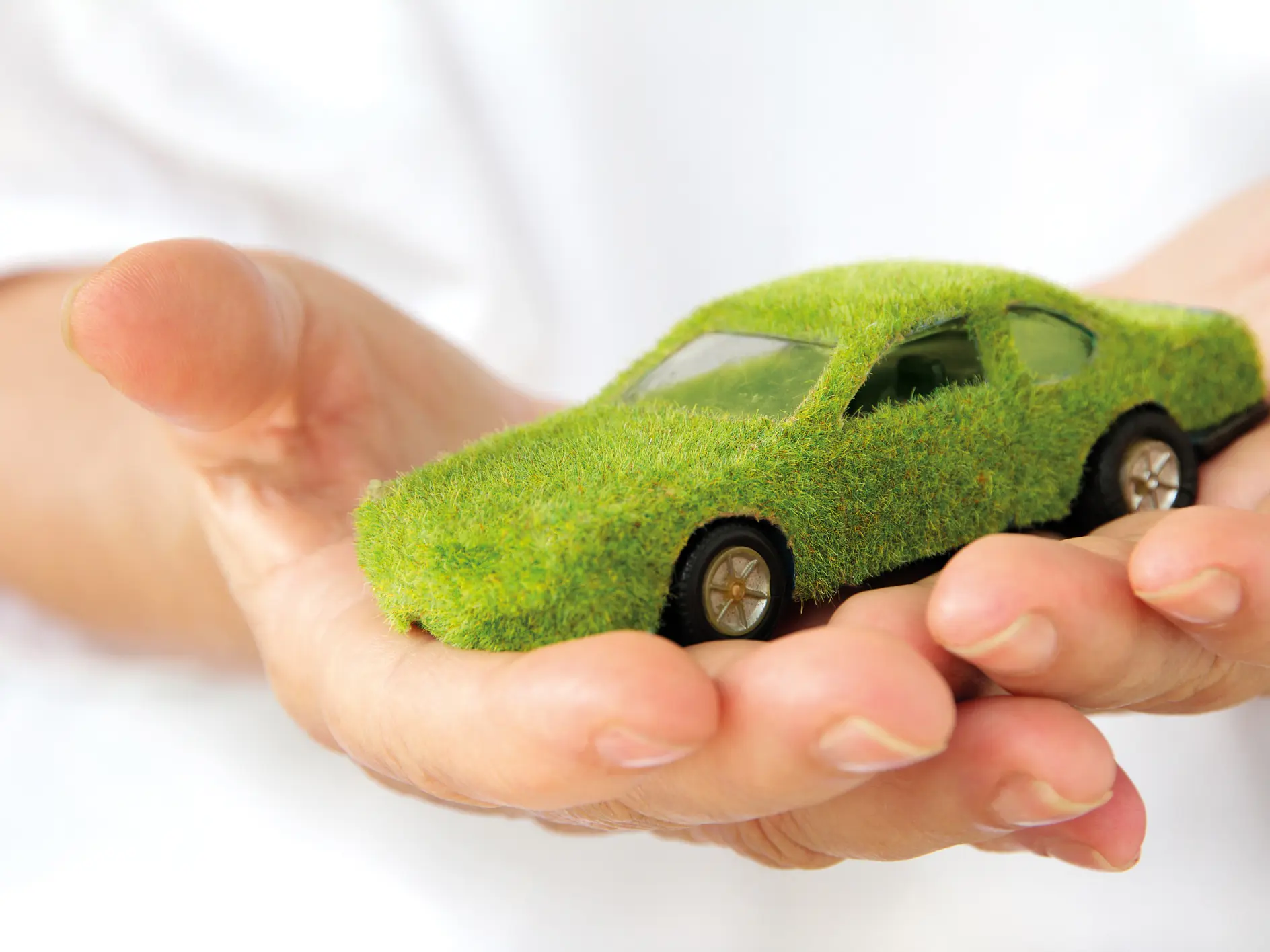 Hands holding a small car model covered in green grass-like material, symbolizing eco-friendly or sustainable automotive concepts. (This text has been generated by AI)