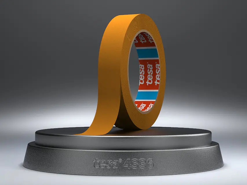 A roll of adhesive tesa tape is placed on a round pedestal. The tesa tape is brown, with visible red and blue branding inside the roll. The pedestals front has the text tesa 1936 engraved on it. The background is a neutral gray.