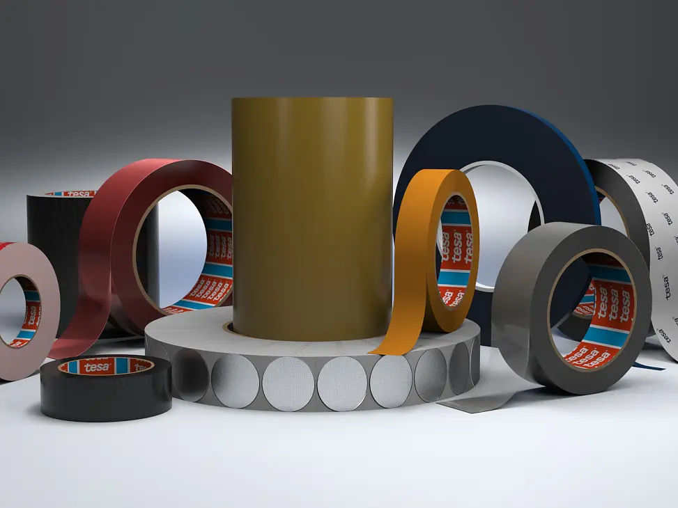 A variety of adhesive tesa tape rolls are displayed, including red, green, black, orange, blue, and white colored tesa tapes. Some rolls stand upright, while others lie flat. Circular, white stickers are also arranged among the tesa tapes.