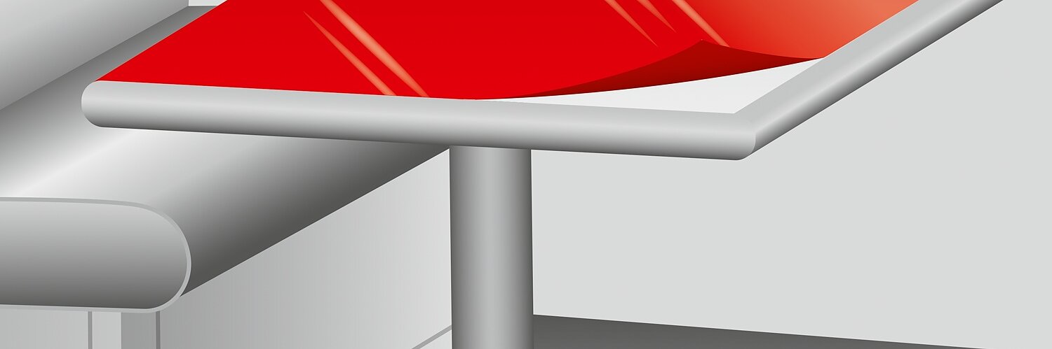 A graphic illustration of a metallic table with a red rectangular top. The table is positioned beside a white, cushioned booth seat in a minimalist setting. The surface of the table reflects light, giving it a glossy appearance. (This text has been generated by AI)
