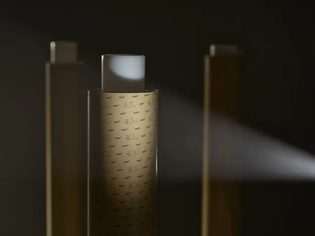 three vertical rectangular objects with perforated surfaces in a dark setting, one emitting a focused beam of light to the right