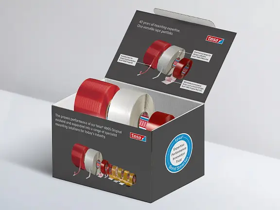 A box with several rolls of tesa tape in various colors and types; lid open to show info and images; box on a plain surface. (This text has been generated by AI)