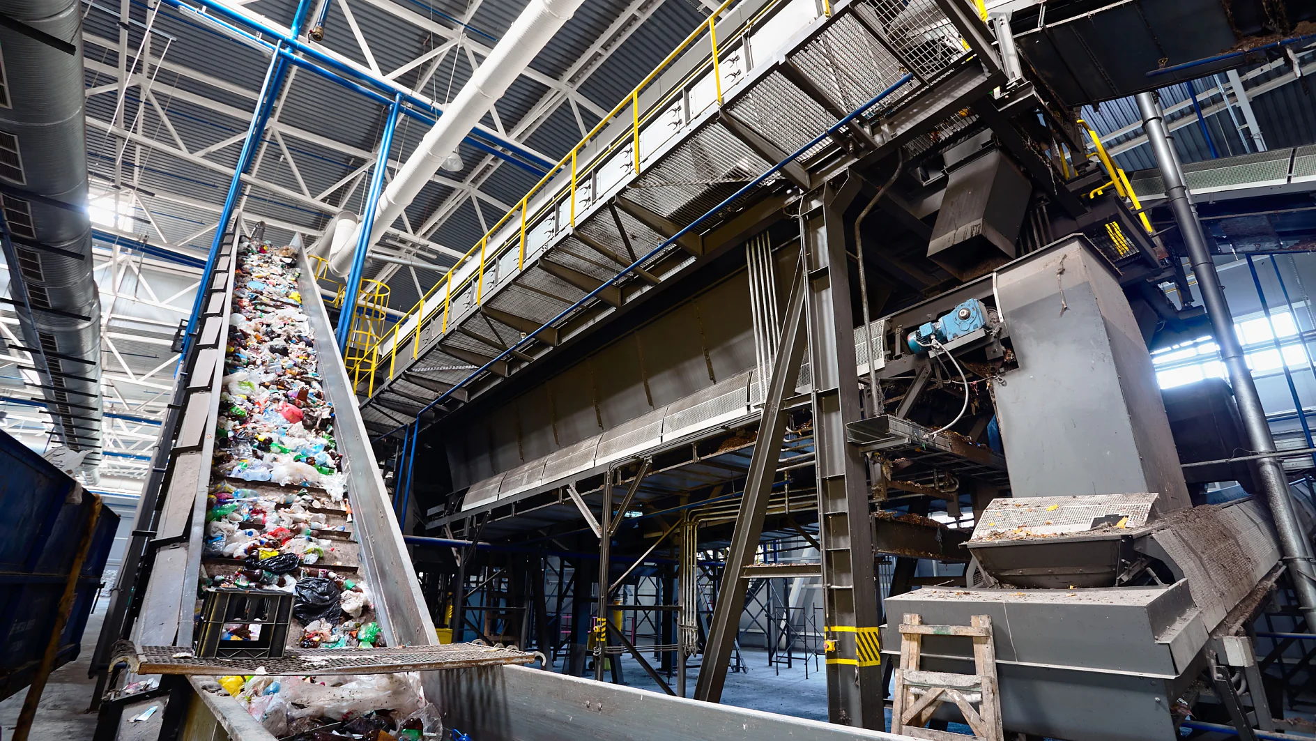 Wide angle view at recycling plant conveyor belt transports garbage inside drum filter or rotating cylindrical sieve with trommel