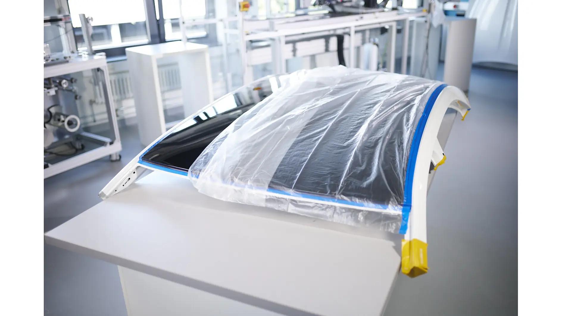 tesa tape securing plastic sheet over car roof panel in bright automotive workshop for paint protection (This text has been generated by AI)